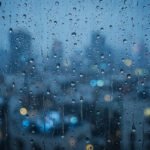Raindrops streaking down a windowpane with a blurred blue city glowing behind, echoing the quiet sadness of these breakup quotes.