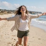 Joyful person dancing alone on a sunny beach with arms wide open, for single life quotes.
